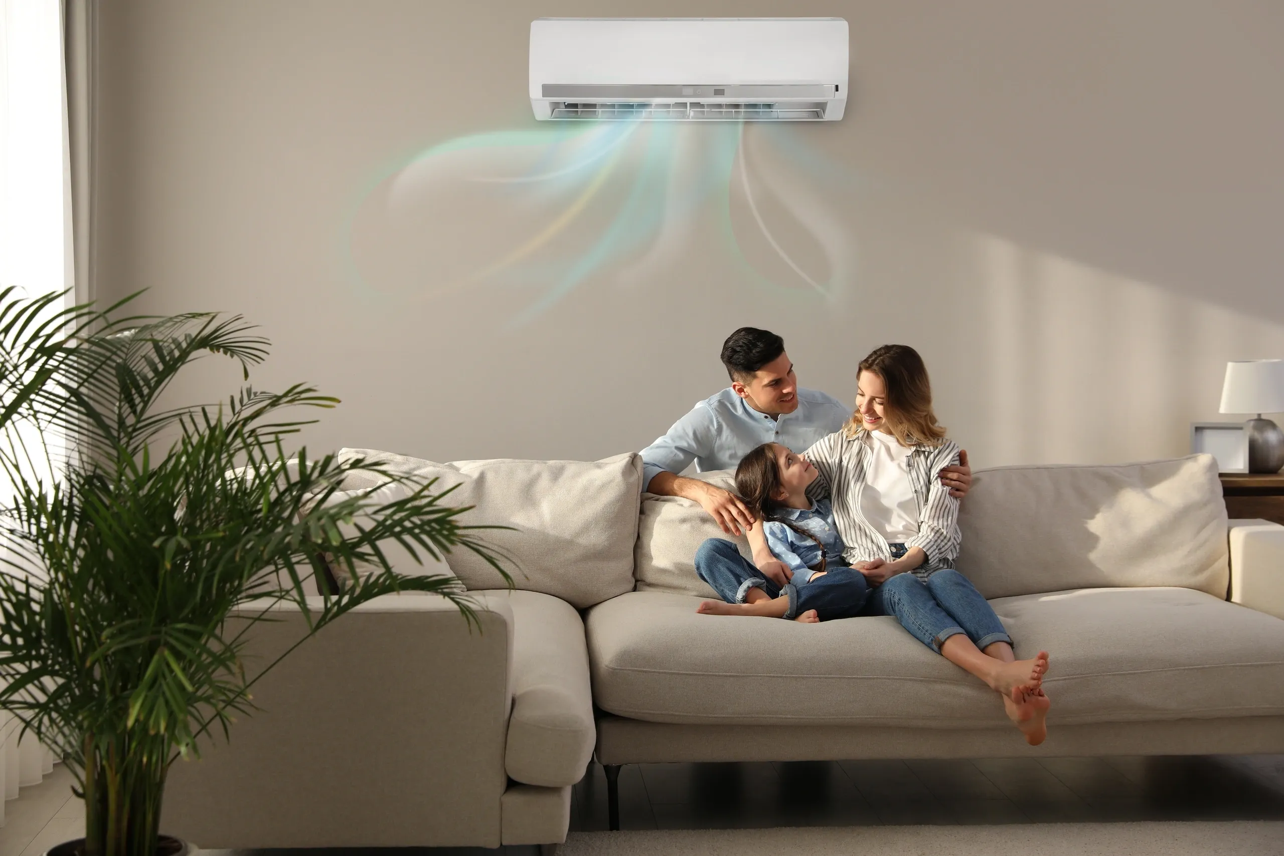 A family relaxes on a sofa under a wall-mounted air conditioning unit.