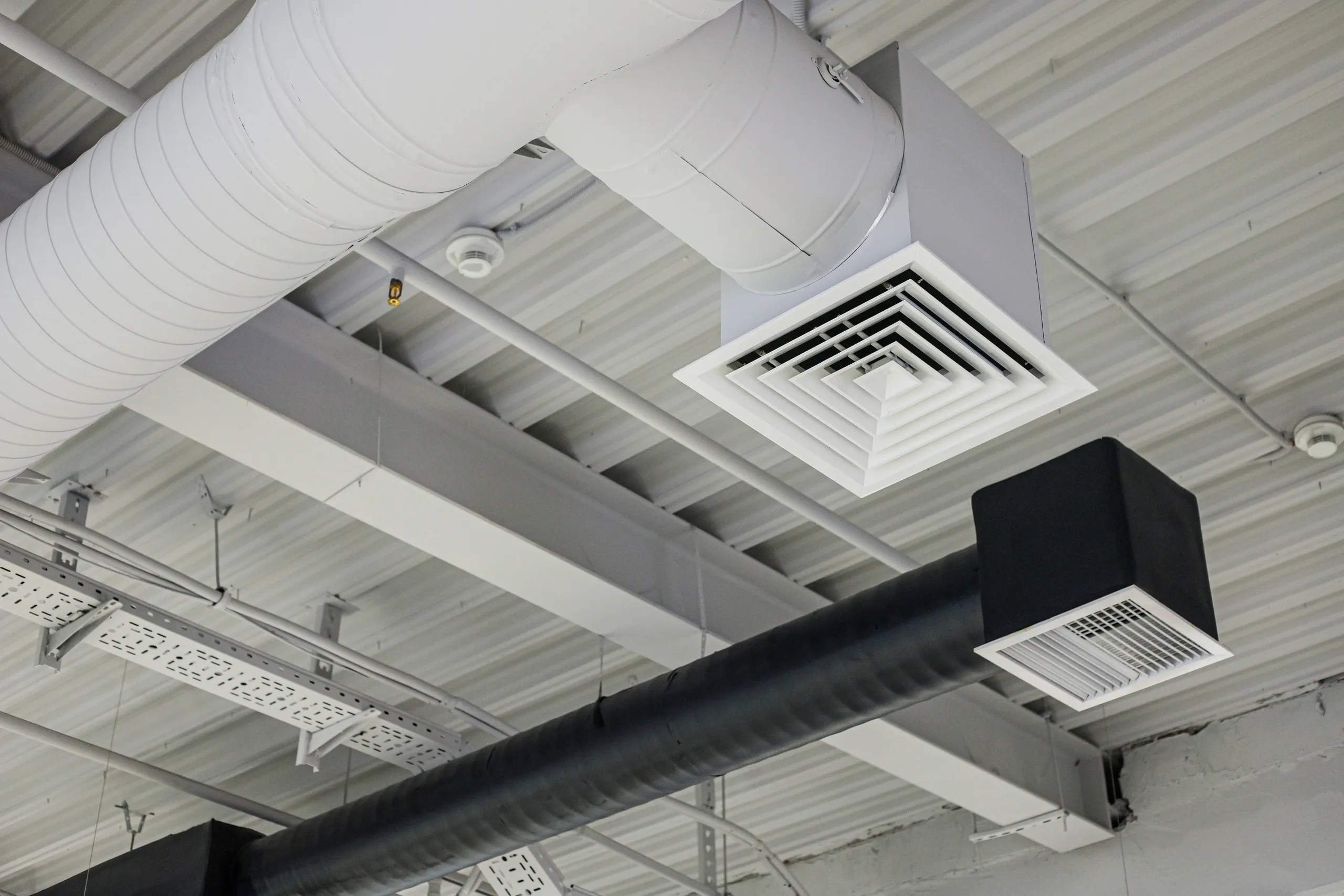Close-up of industrial-style ventilation ducts and grilles on a ceiling.