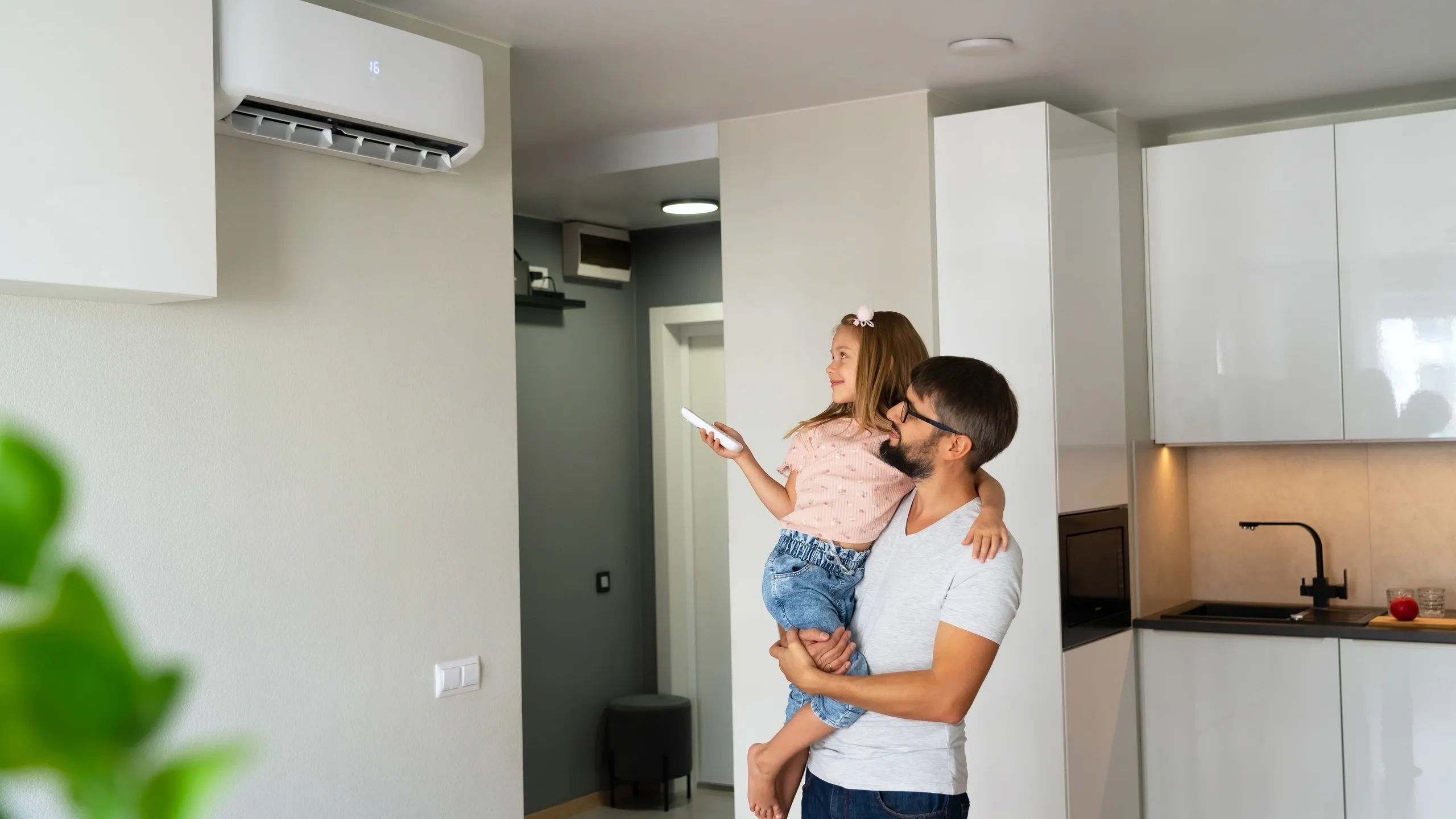 A man holds a child while looking at an indoor air conditioning unit in a modern room.