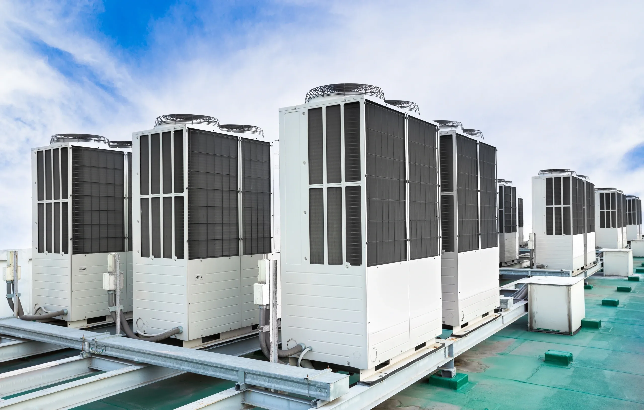 A row of large commercial rooftop HVAC units under a partly cloudy sky.