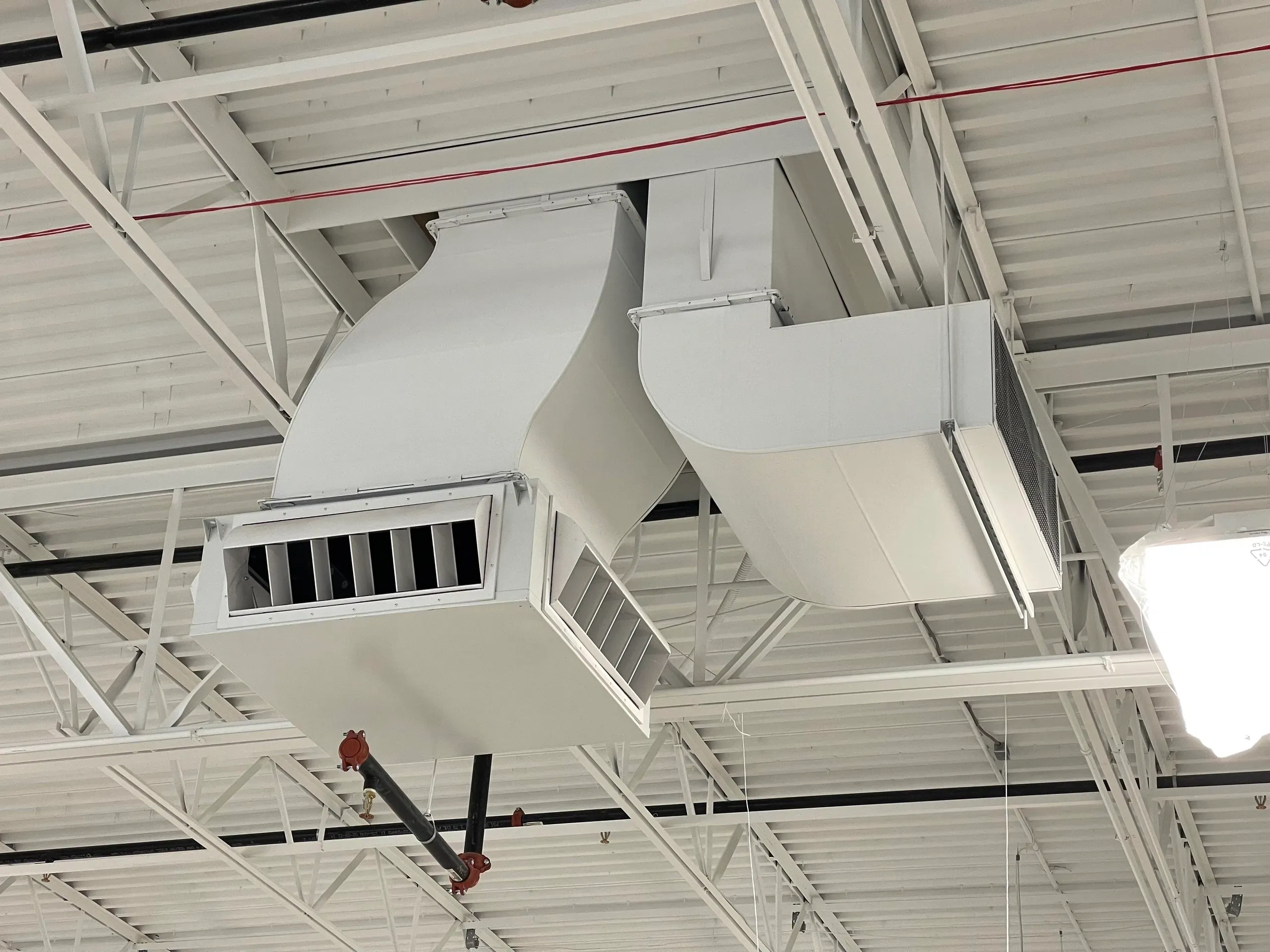 White industrial ductwork and vents are mounted on a ceiling.