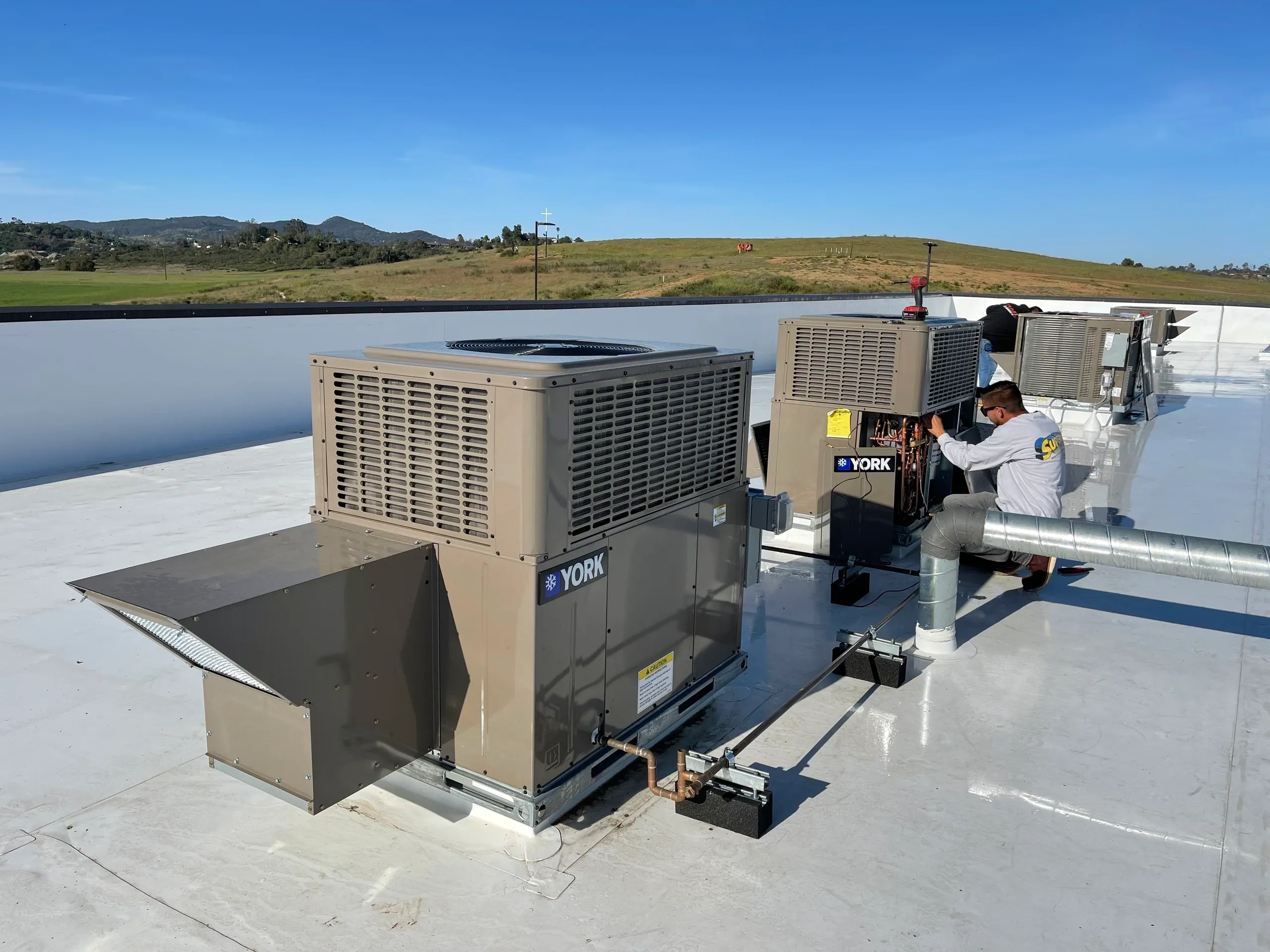 Multiple commercial rooftop HVAC units and ductwork under a clear sky.