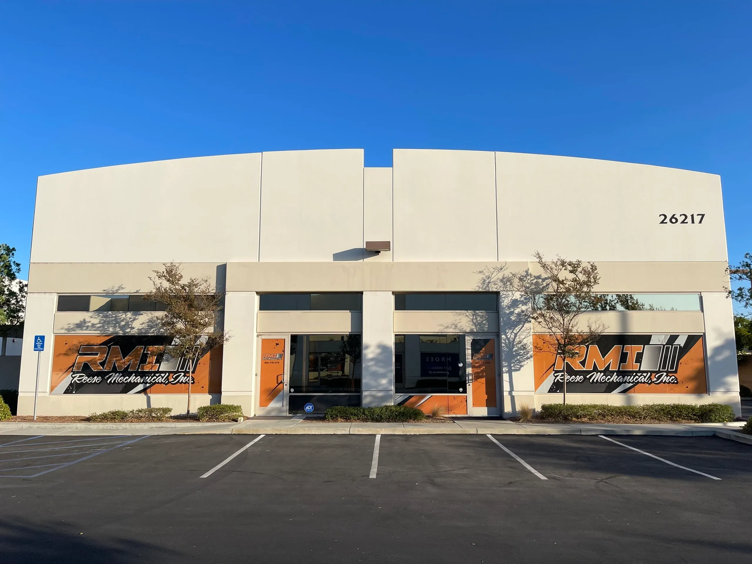An empty commercial building with a large parking lot under a clear sky.